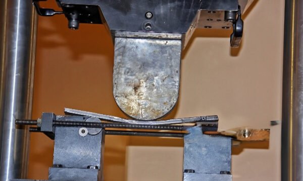 Metal rod being bent by a flexural testing machine to determine its mechanical properties.